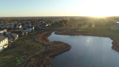 Reverse-dolly-aerial-shot-of-pond-and-residential-neighborhood-at-sunrise