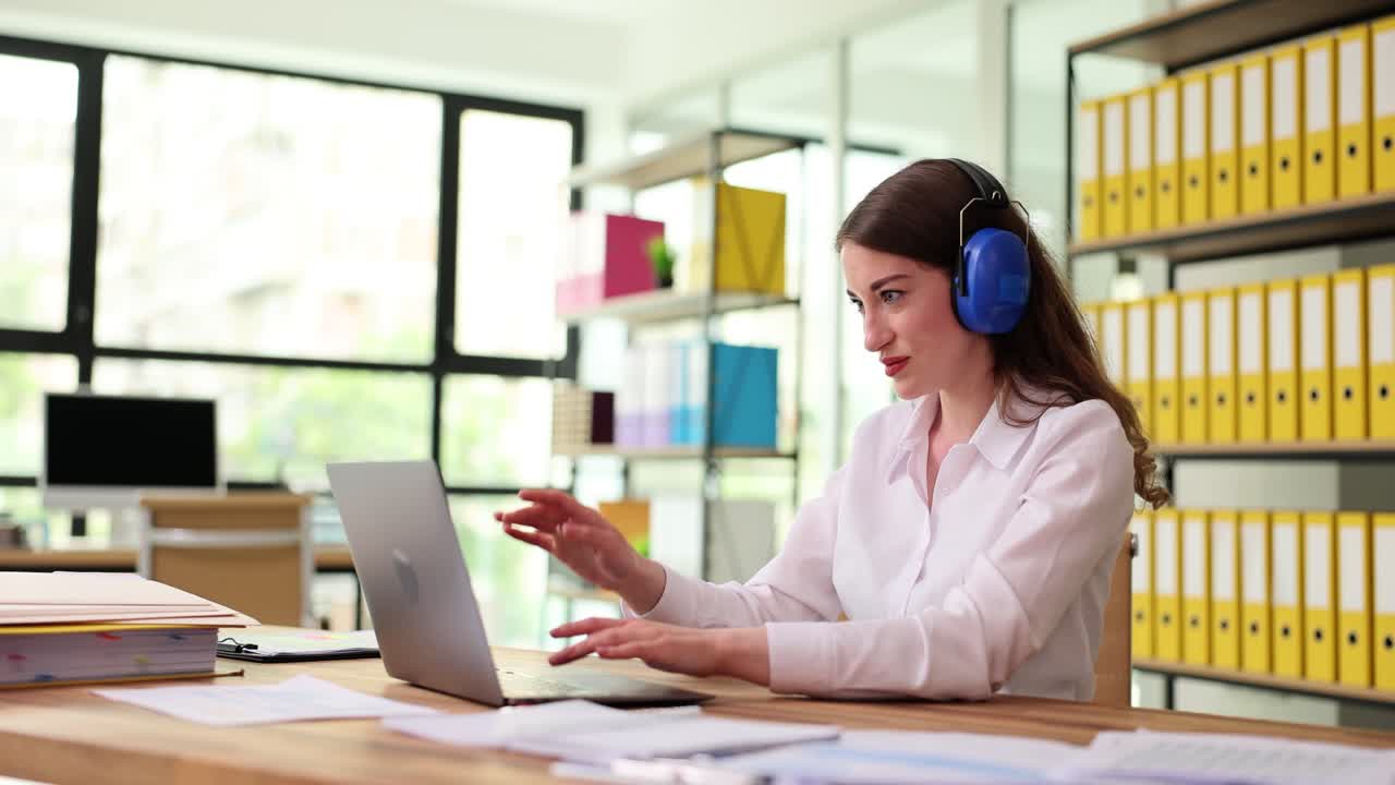 Woman working on laptop with blue headphones in an office