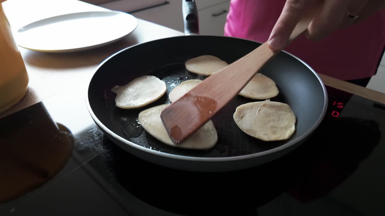 Close-up of pancakes being cooked on a stovetop skillet and flipped with a wooden spatula in a home kitchen setting. Perfect for cooking, breakfast, or homemade food content