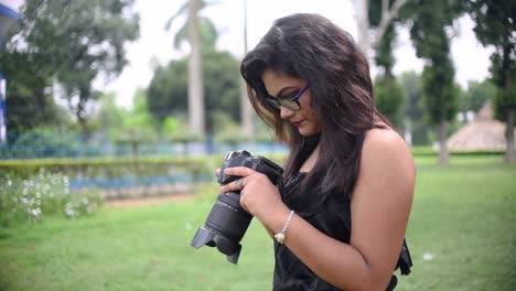 a tourist asian girl takes photos with a dslr camera and checks the photos in camera display at a nature park