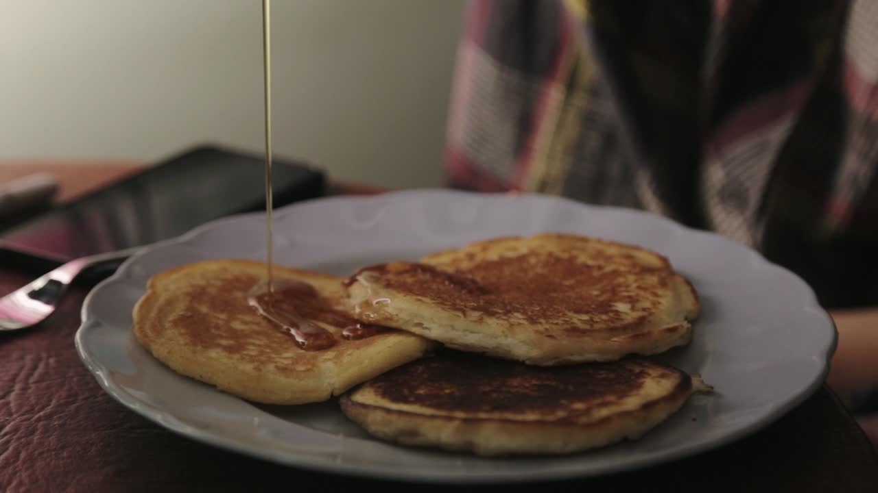 extendiendo lentamente el jarabe de arce en panqueques - primer plano
