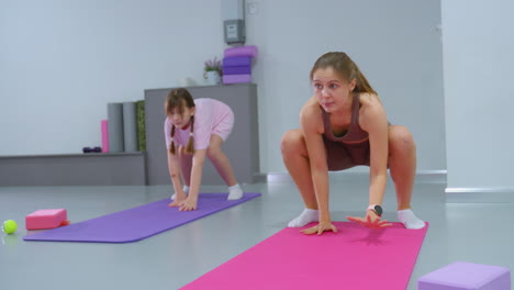 gym trainer demonstrates a backward movement exercise on mat with hands locked as young child follows her lead, mimicking every motion with focus and determination