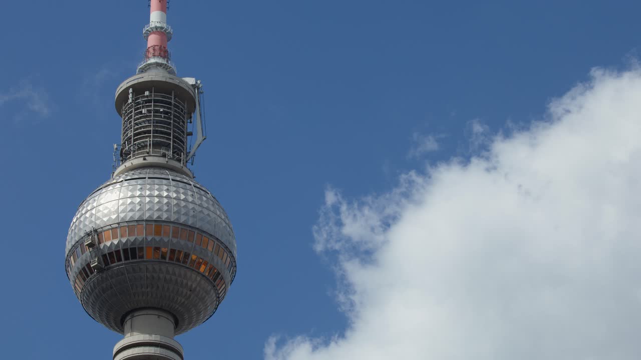 Camera tilts up Fernsehturm tower with clouds, bright daylight, clear architectural details, smooth movement