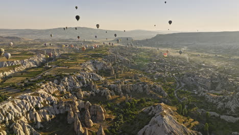 Göreme-Turkey-Aerial-v71-sunrise-landscape-captured-rock-formation-of-plateaus,-fairy-chimney-and-ancient-town-with-cave-dwellings-with-hot-air-balloons-in-the-sky---Shot-with-Mavic-3-Cine---July-2022