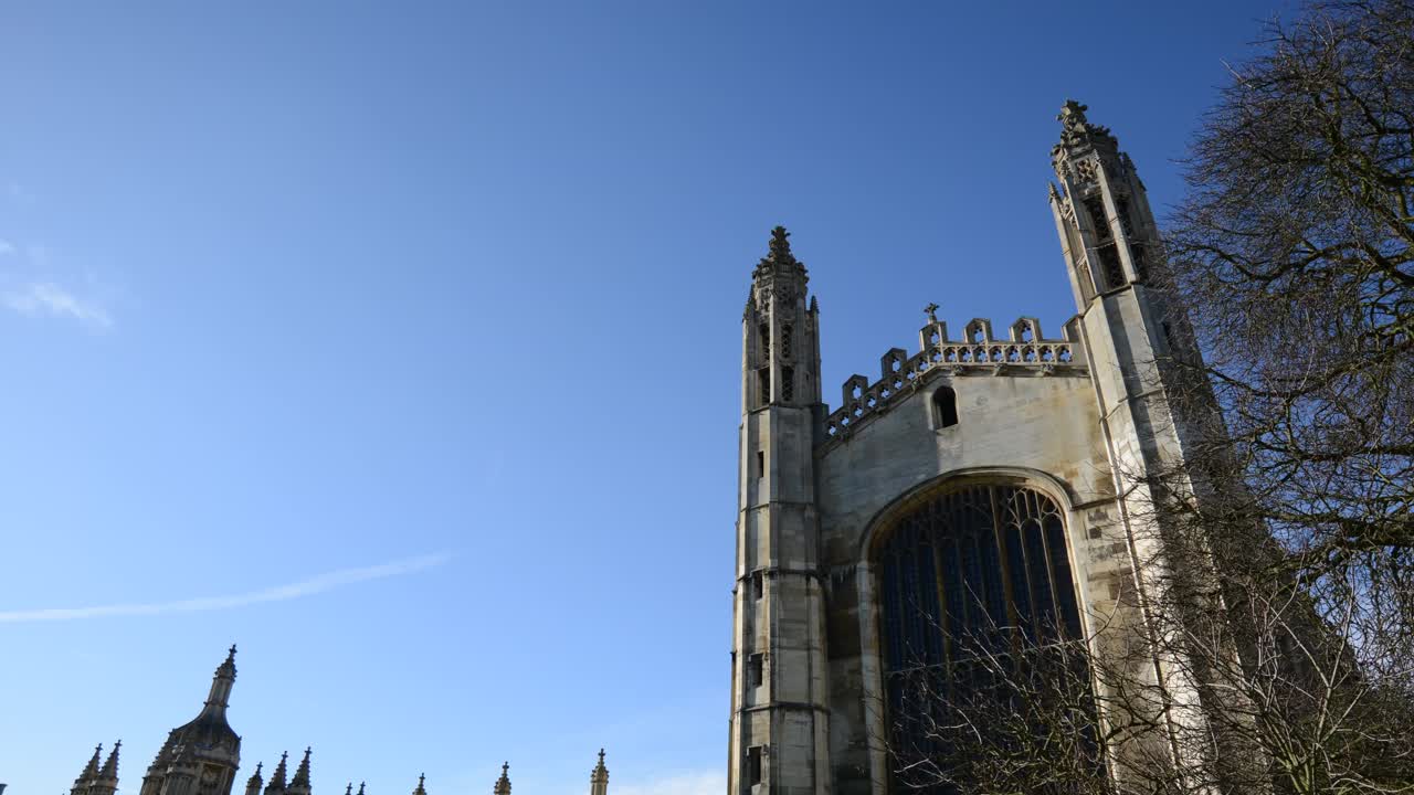 Drone hyperlapse of King's College Chapel, Cambridge, showcasing gothic architecture against a clear blue sky. Majestic towers rise, while bare winter trees add elegance, blending history with nature