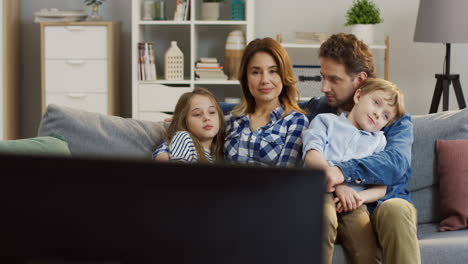 family with children sitting on the sofa in the living room and watching tv