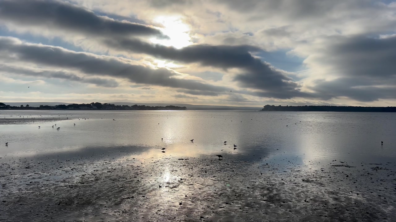 Calm tidal water at Morecambe Bay reflecting dramatic cloud filled sky with soft light and wet sand creating peaceful coastal landscape