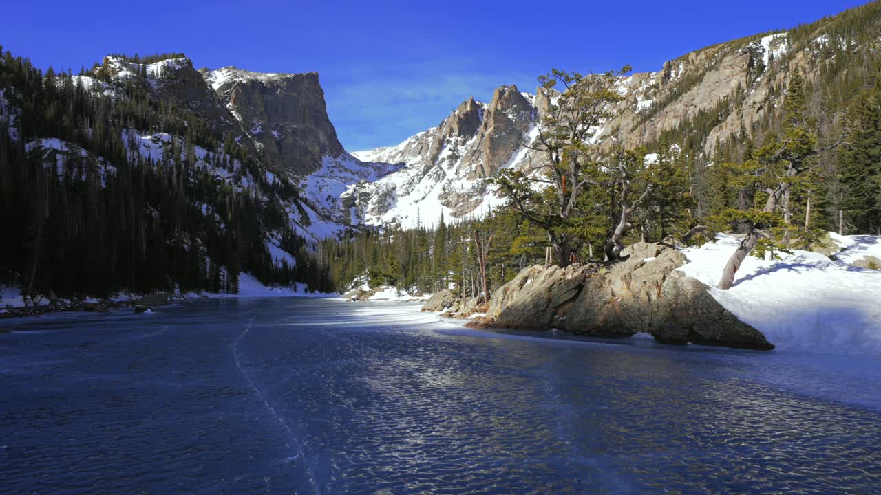 Dream Lake, Colorado, Rocky Mountain nasjonalpark (RMNP). Emerald Lake, Estes Park. Bear Lake tursti. Solrik blå himmel. Hallett Peak og Flattop-fjellene. Snøfokk og vindfullt. Frossen blå is, skyggelagt, zoomet inn.