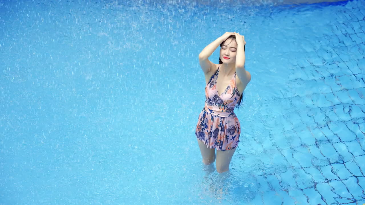 Vrouwelijke toerist in bikini geniet van een verfrissende douche bij watervallen in een tropisch resort met zwembaden met warmwaterbronnen en een thermaalwaterpark. Ze geniet van de zon en dompelt haar hand in het water.