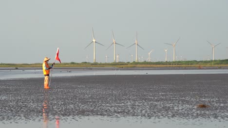 worker with flag signaling near wind turbines in a mudflat