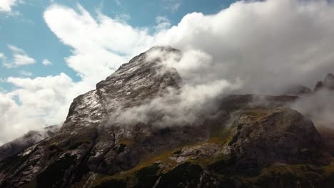 High-Dolomite-peak-in-northern-Italy-with-rocky-cloudy-top-during-a-clear-winter-day,-Aerial-drone-dolly-out