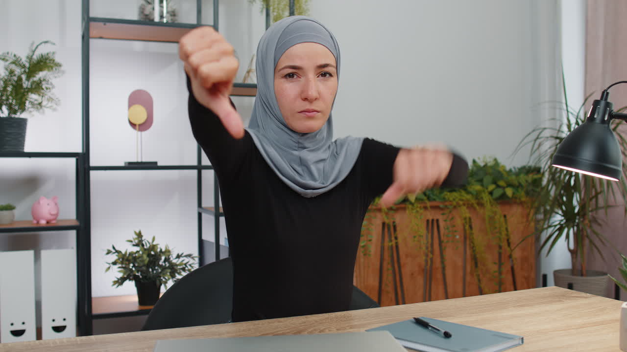Upset young muslim business woman showing thumbs down, dislike, discontent, disapproval, bad work