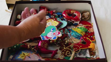 a hand reaches into a box of christmas tree ornaments to select what will go on the tree