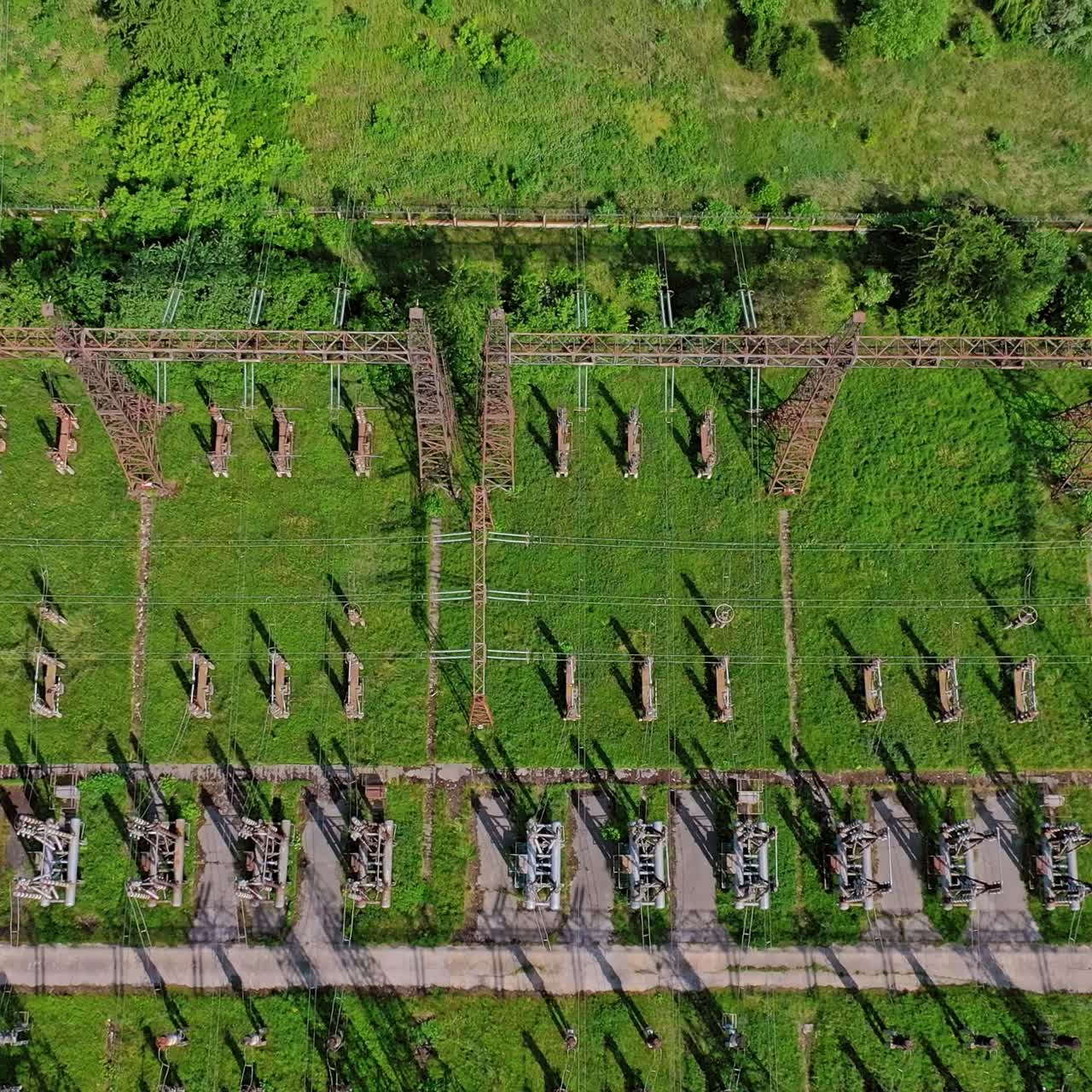 High voltage lines on green field. Flight over power transmission lines. Huge territory with steel pillars for electricity. Top aerial view.