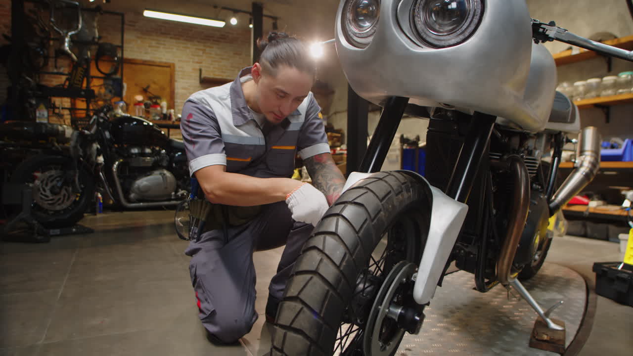 Repairman Examining Wheel of Motorcycle and Smiling at Camera
