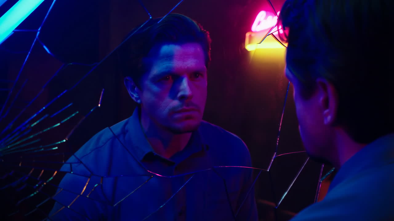 Uomo che guarda il suo riflesso in uno specchio rotto con luci al neon