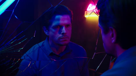 man looking at his reflection in a broken mirror with neon lights