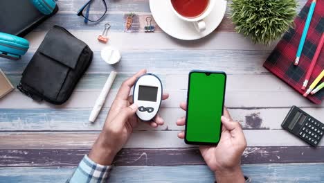 la mano del hombre sosteniendo el medidor de glucosa y el teléfono inteligente en la mesa
