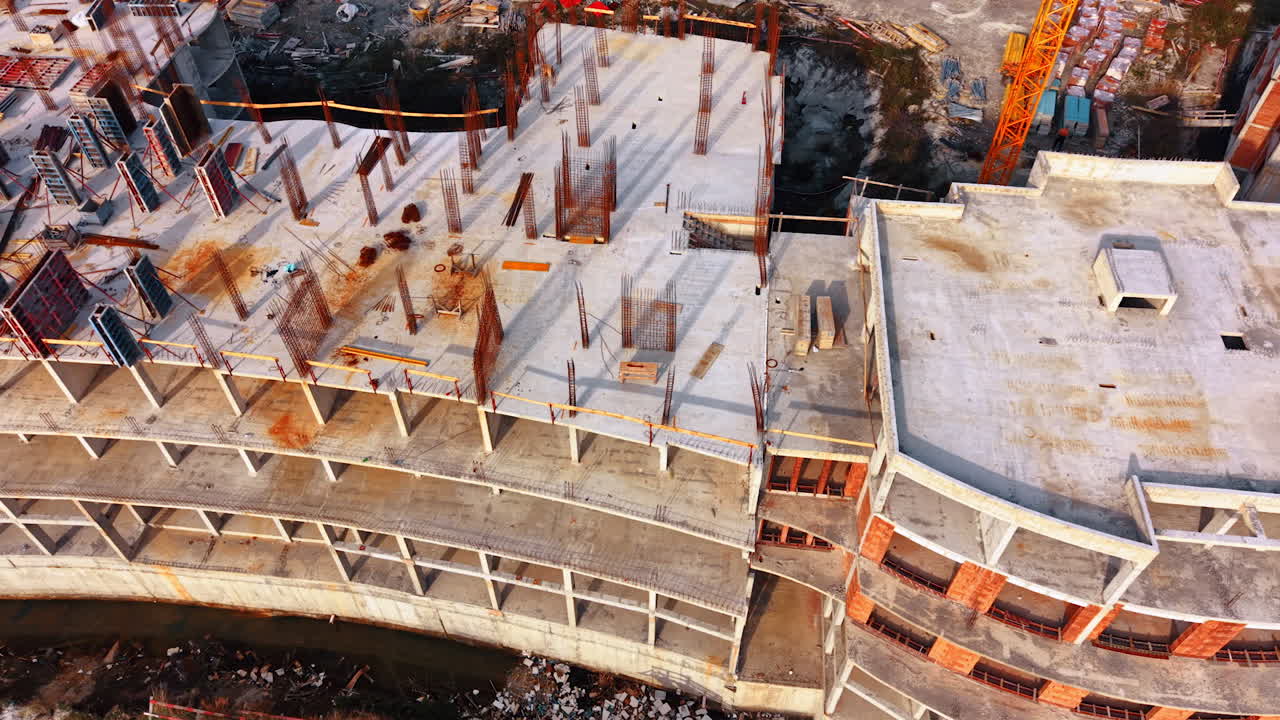 Workers are busy at a construction site where a large building is being erected. Scaffolding and metal supports are visible along with concrete slabs being placed
