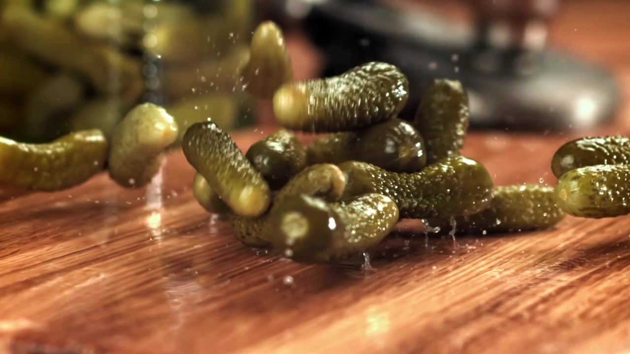 Chute de cornichons au ralenti sur une table en bois.