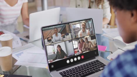 African-american-man-using-laptop-for-video-call,-with-diverse-business-colleagues-on-screen