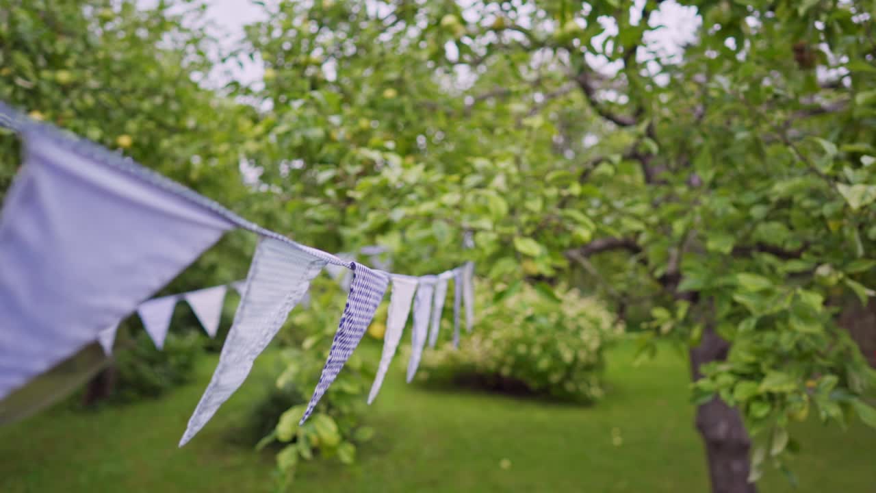 A row of party decoration flags in an apple orchard. Concept of a birthday and a festive summer garden party.