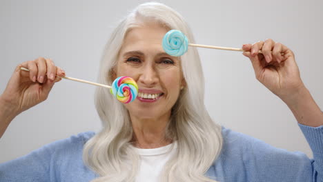 happy senior woman smiling in studio. old lady playing with candy indoors.