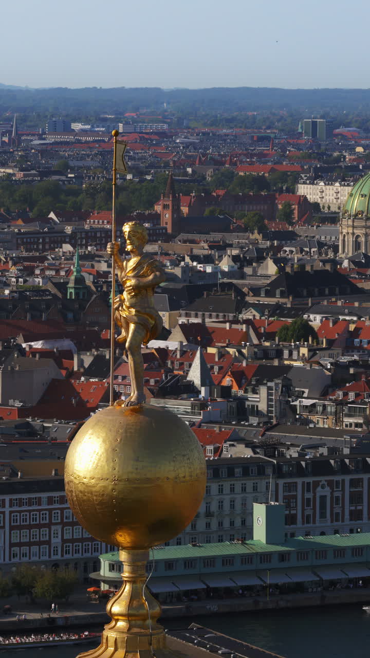 Aerial drone view of the golden statue atop a sphere on the Church of Our Saviour overlooking the Copenhagen skyline, with Frederik's Church dome in the background in Denmark. Vertical