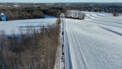 Snow-covered-landscape-with-patterned-fields,-trees-and-small-village-of-USA-in-background