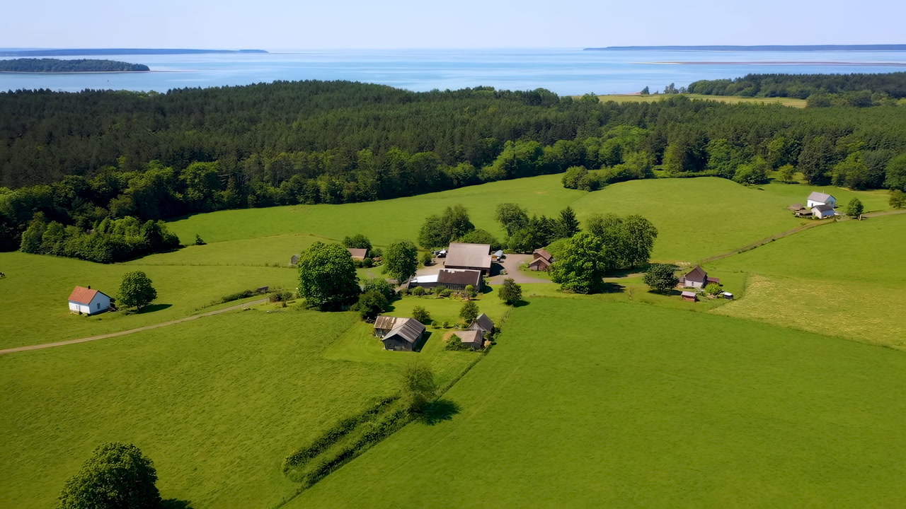Aerial Green Farmland With Coastline Showing Small Village Cluster Of Traditional Farmhouse And Barns, Rolling