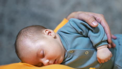 beautiful infant boy sleeping sweetly in father's hands. adorable baby resting peacefully. grey backdrop. close up.
