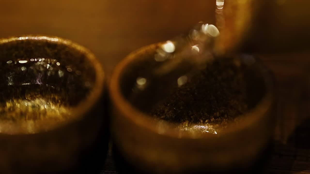 Close-up of liquid being poured into two brown ceramic cups on a wooden surface.