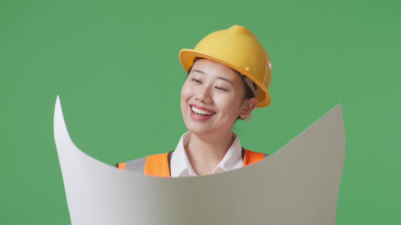 녹색 스크린 배경 스튜디오에 서 있는 동안 안전 헬을 착용 한 아시아 여성 엔지니어의 가까운 모습