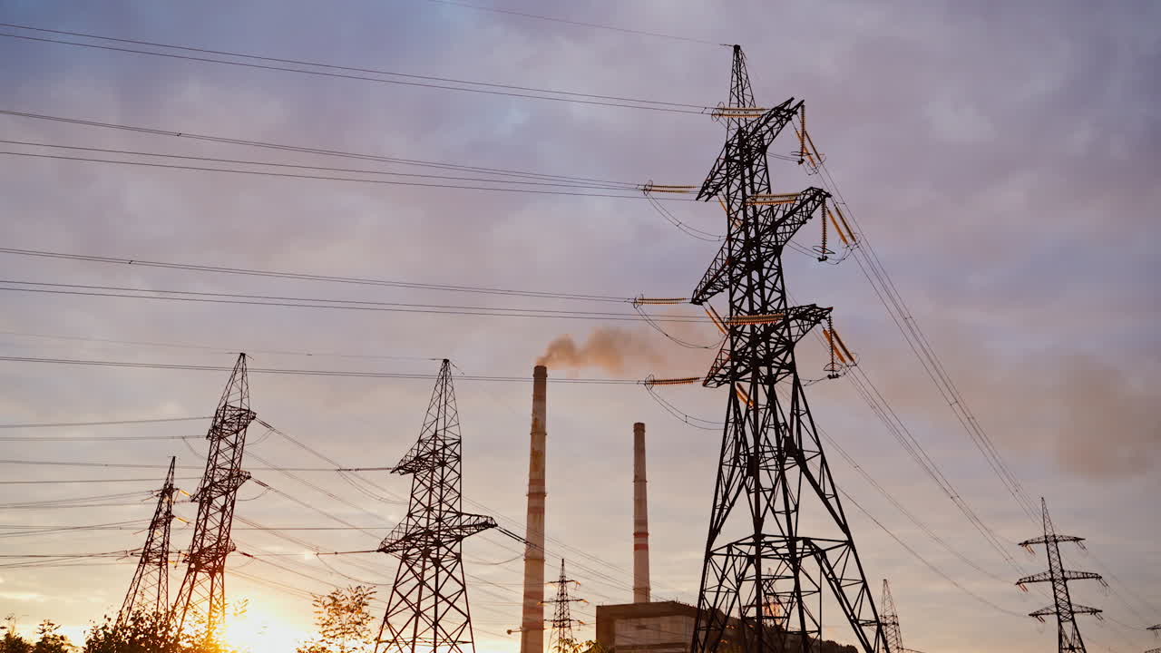 Electricity pylons against orange and yellow sunset. Selective focus. Video from the side.
