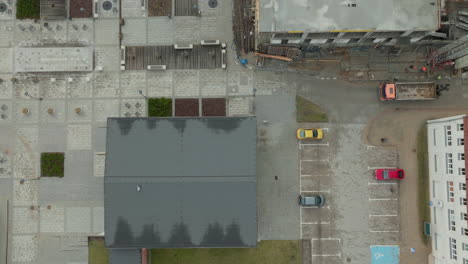 Urban-landscape-from-a-unique-aerial-perspective,-highlighting-the-intricate-patterns-of-construction-sites,-textured-rooftops,-and-parked-vehicles-that-compose-the-daily-rhythm-of-city-life