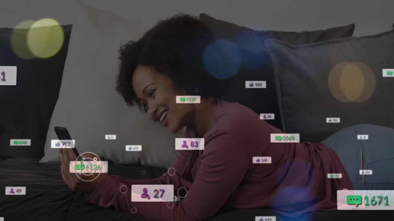 Animation of social media icons over african american woman having a videocall on the couch at home
