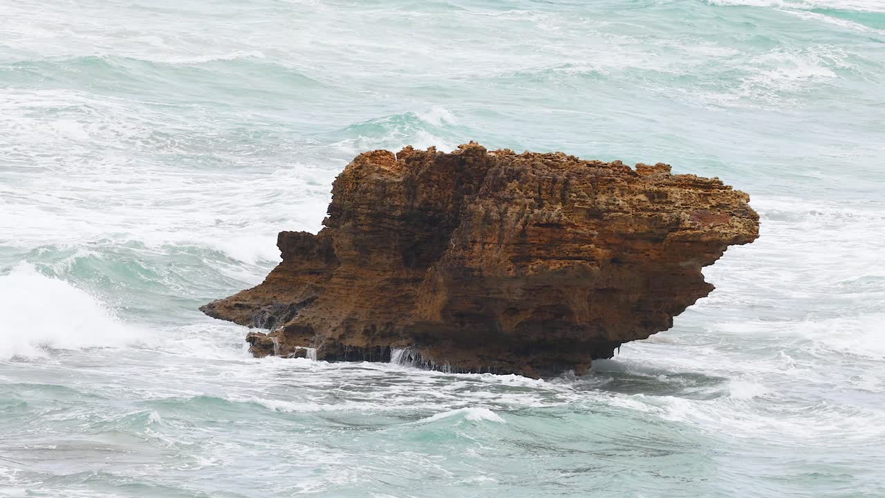 A solitary rock withstands powerful ocean waves under overcast skies along Australia's Great Ocean Road