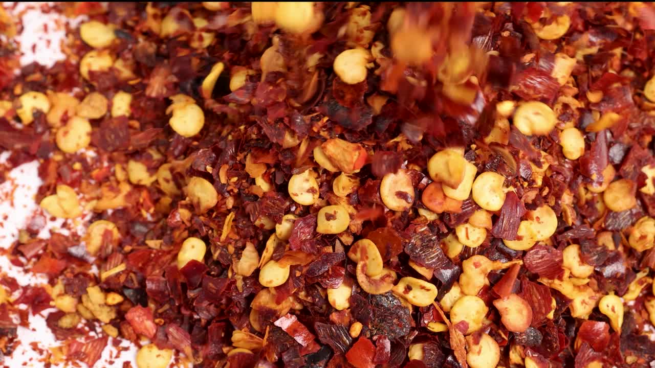 Dried chili flakes cascade onto a surface in a macro close-up, highlighting texture and vibrant colors under bright lighting