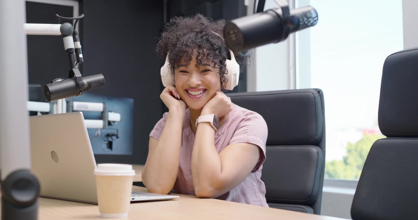 Donna afroamericana che prepara un podcast, digita sul laptop, sistema le cuffie e sorride.