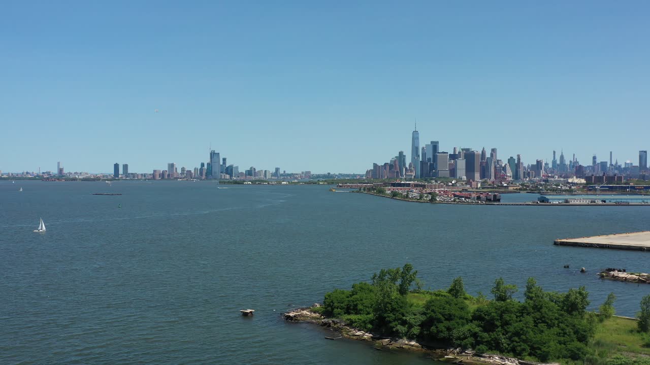 작은 흰색 범선이 보이는 뉴욕 만 상공의 맨하탄 하부를 향해 느린 공중 돌리 샷