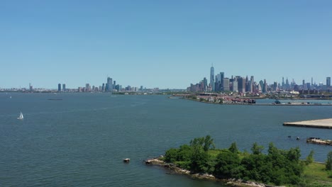 Langsame-Luftaufnahme-Eines-Dollys-In-Richtung-Lower-Manhattan-über-Der-Upper-New-York-Bay-Mit-Einem-Kleinen-Weißen-Segelboot-Im-Blick