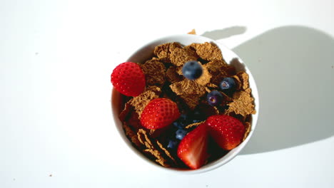 fresas y arándanos que caen en un cuenco de cereales de trigo