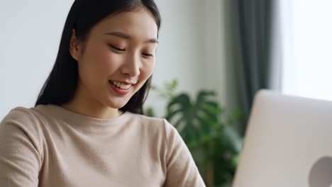 a young woman engaged in online communication, smiling while connecting through her laptop in a bright, cozy indoor environment surrounded by greenery
