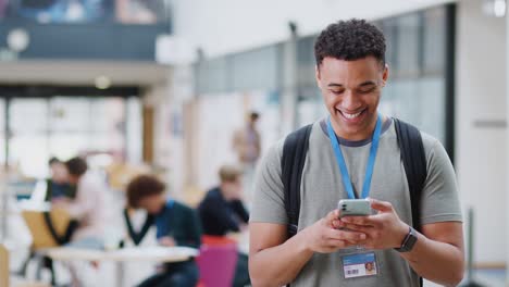 smiling male college student checking mobile phone in busy communal campus building