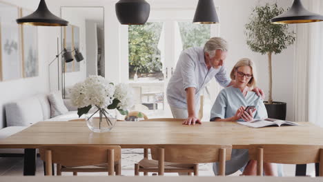 Pareja-Mayor,-En,-Comedor,-En-Casa,-Mirar,-Y,-Teléfono-Móvil,-Juntos