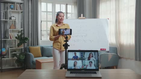 asian female teacher shoots video by smartphone camera and having video call on laptop while teaching math at home