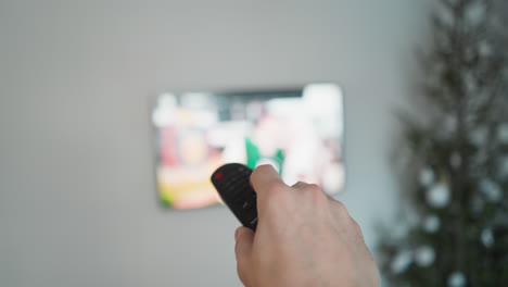 hand holding remote control in front of tv, christmas tree in blur, pov shot