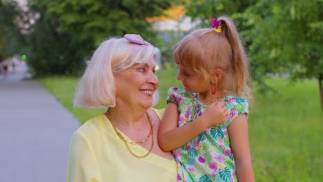 little granddaughter child embracing kissing with her grandmother in park, happy family relationship