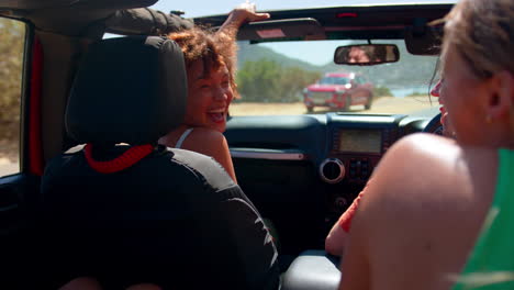 group of laughing female friends having fun in open top car on road trip