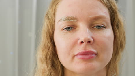 close-up of client wearing nose ring during beauty session with visible cream applied on one eyebrow while the other remains untouched, showing contrast in eyebrow treatment process in clean salon